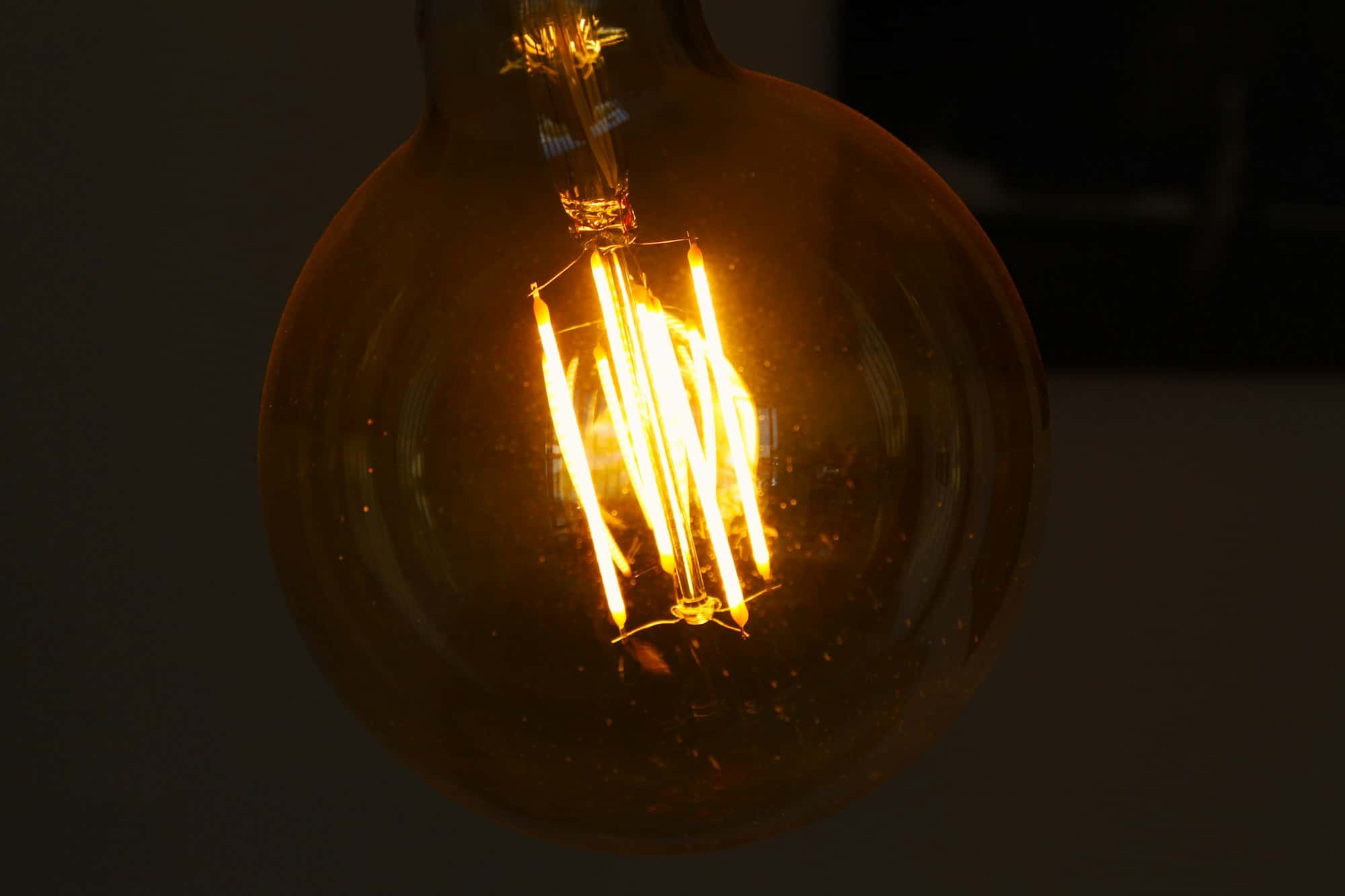 A clear filament bulb glowing warm in the dark
