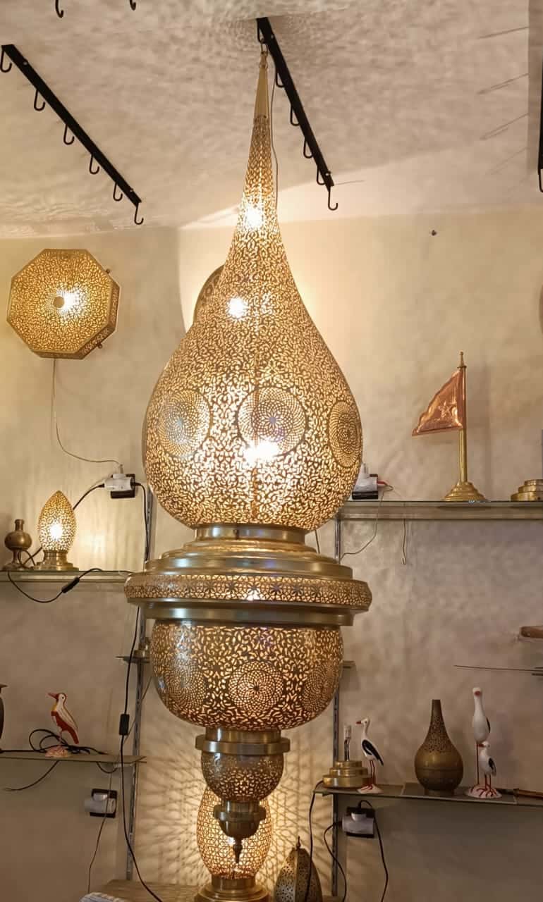 Tall teardrop-shaped hand-pierced brass Flamla pendant, lit, in the showroom