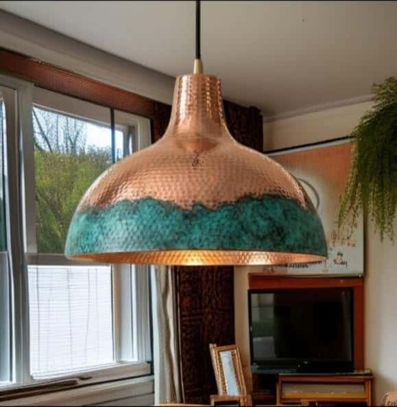 Hammered copper bell pendant with a blue-green verdigris band, lit, hanging by a window