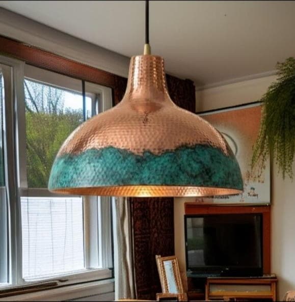 Hammered copper bell pendant with a blue-green verdigris band, lit, hanging by a window