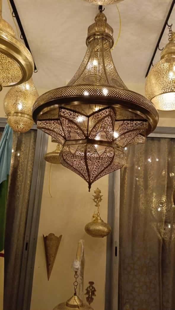 Hand-pierced brass star chandelier, lit, hanging in the workshop