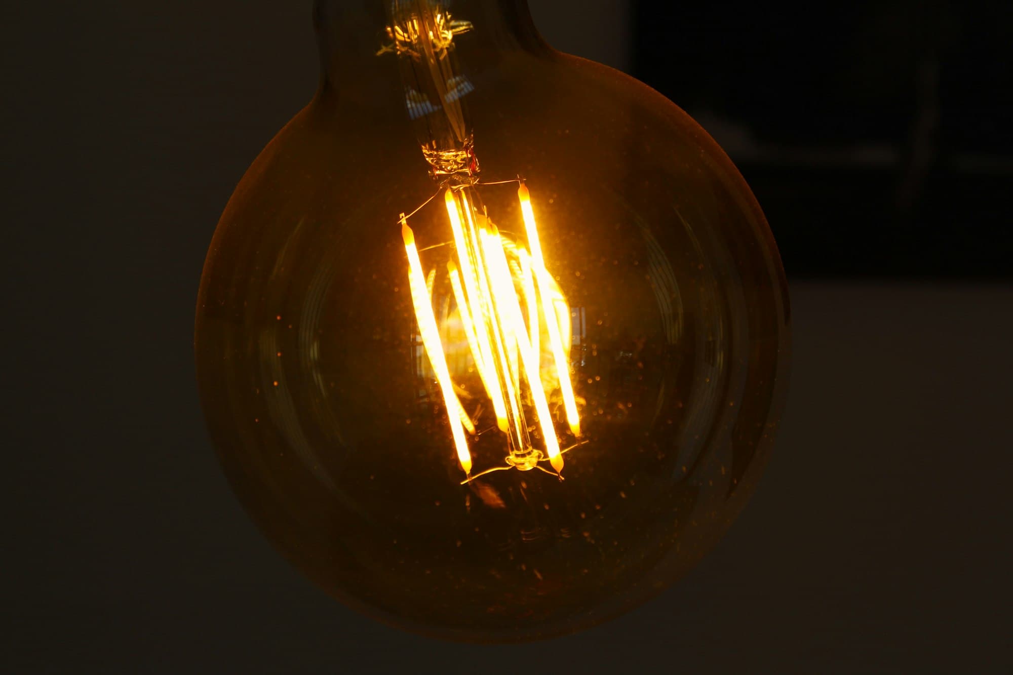 A clear filament bulb glowing warm in the dark