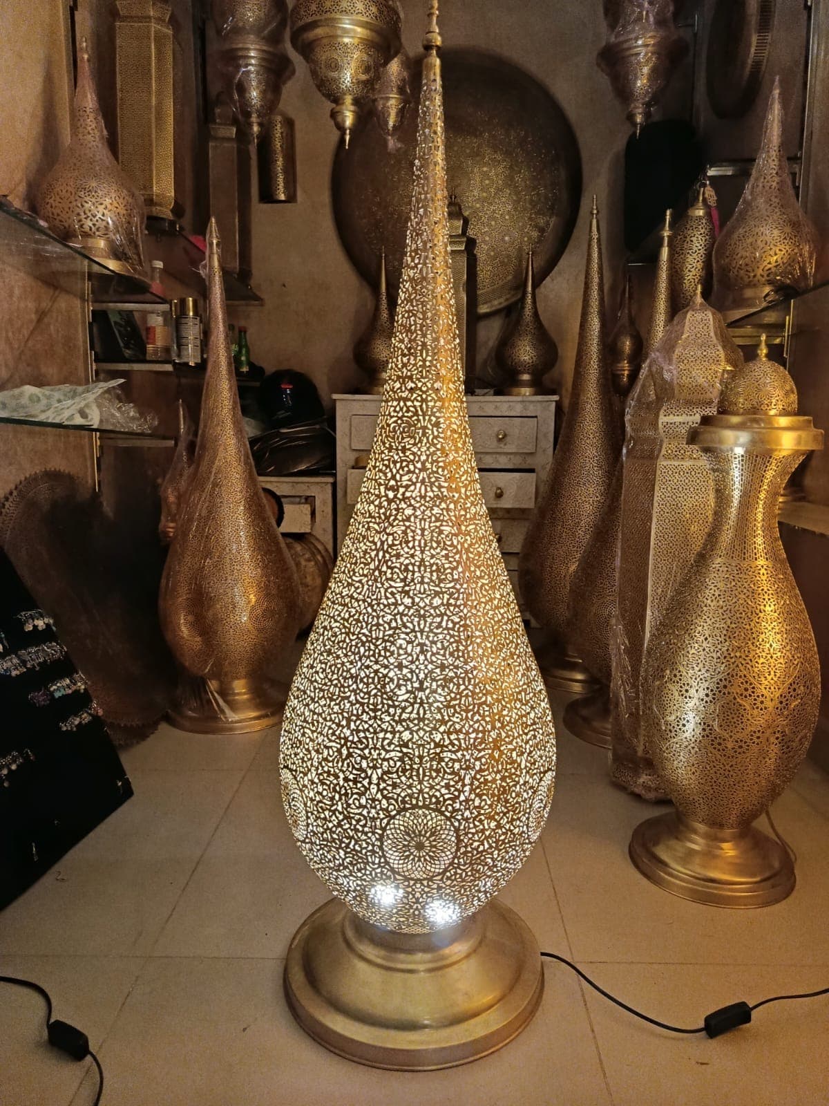 Tall hand-pierced brass teardrop floor lamp, lit, in the workshop